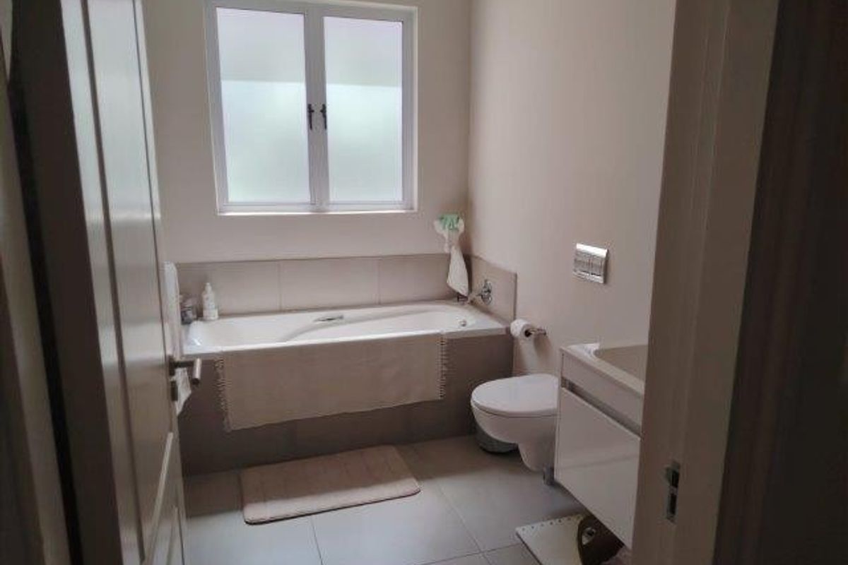 A clean and modern bathroom featuring a built-in bathtub, wall-mounted toilet, and a sleek vanity cabinet with neutral floor and wall tiling.