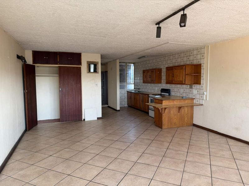 Open-plan living and kitchen area featuring tiled flooring, built-in wooden cabinetry, and a functional kitchen layout in need of cosmetic updates.