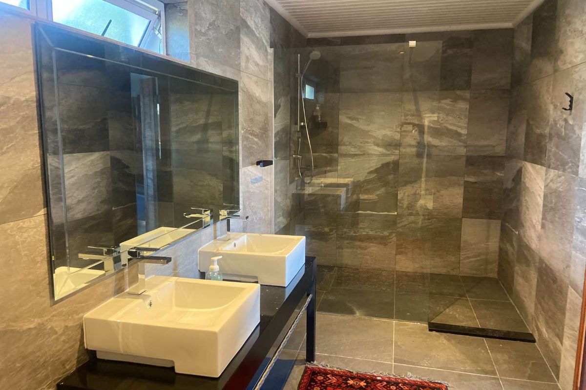 Modern bathroom featuring a double vanity with vessel sinks, a large frameless glass walk-in shower, and floor-to-ceiling grey stone-look tiling.