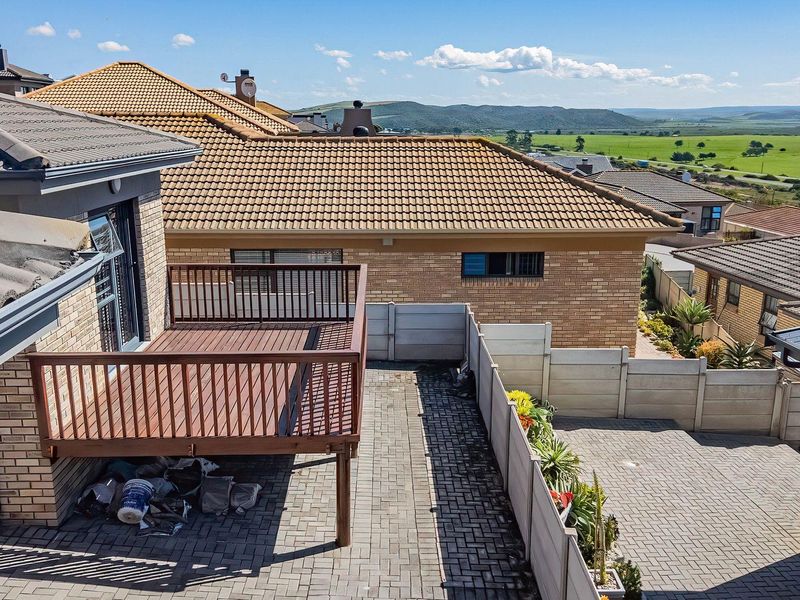 Elevated view of a rear courtyard featuring a raised timber deck, paved surfaces, and precast boundary walls with surrounding residential landscape views.