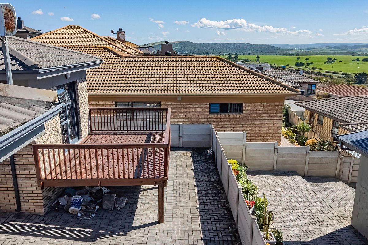Elevated view of a rear courtyard featuring a raised timber deck, paved surfaces, and precast boundary walls with surrounding residential landscape views.