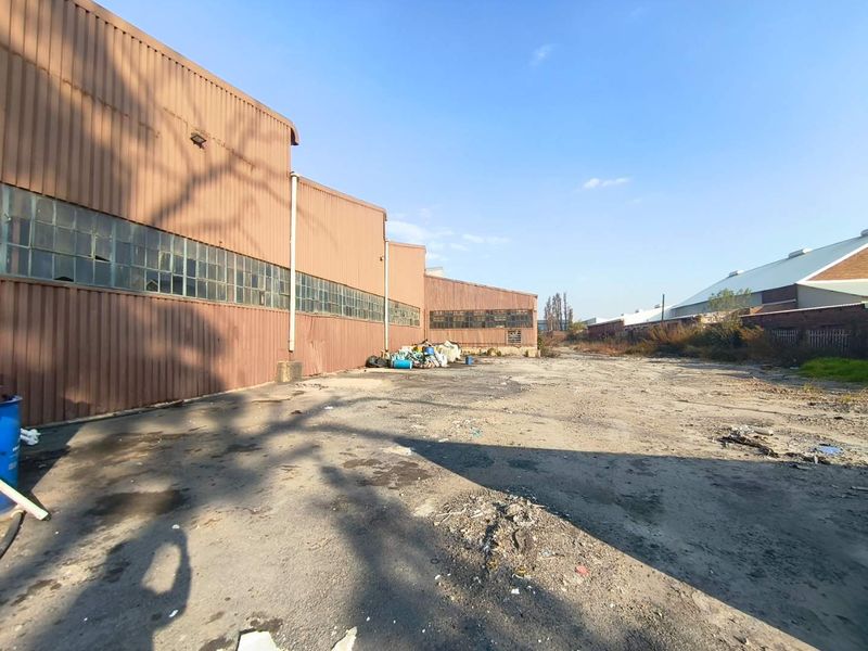Rear industrial yard area featuring corrugated metal cladding, steel-framed windows, and an expansive, weathered asphalt surface suitable for industrial storage or logistics.