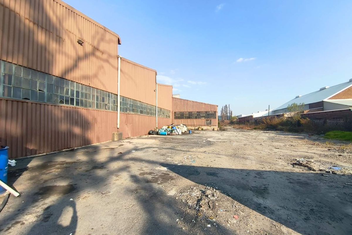 Rear industrial yard area featuring corrugated metal cladding, steel-framed windows, and an expansive, weathered asphalt surface suitable for industrial storage or logistics.
