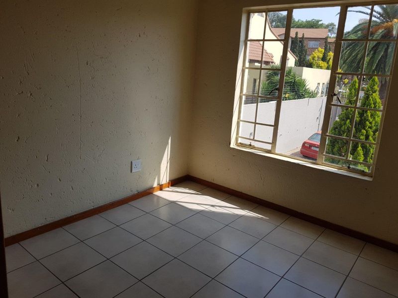 An empty bedroom featuring tiled flooring, textured walls, and a steel-framed window with views of the exterior.