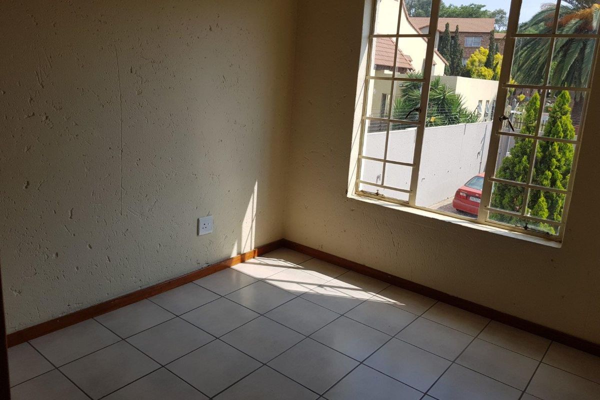 An empty bedroom featuring tiled flooring, textured walls, and a steel-framed window with views of the exterior.