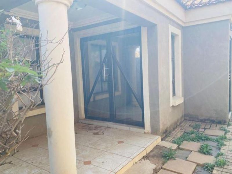 A covered patio area featuring tiled flooring, a structural column, and a sliding glass door entrance, requiring maintenance to the surrounding paved area.