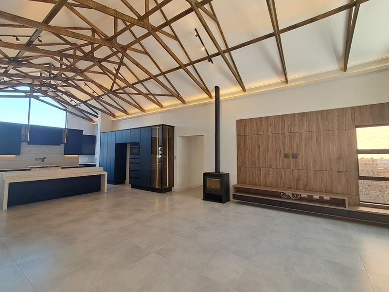 Spacious open-plan living area featuring high vaulted ceilings with exposed timber trusses, a modern kitchen, and a sleek freestanding fireplace.