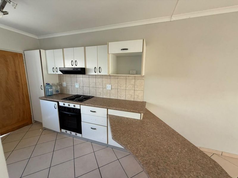 A functional kitchen featuring white cabinetry, laminate countertops, a built-in oven with hob, and tiled flooring, offering a clean space ready for updates.