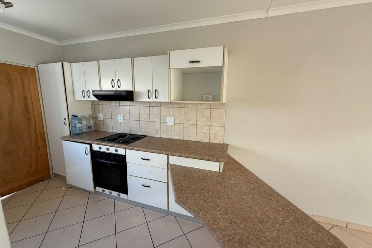 A functional kitchen featuring white cabinetry, laminate countertops, a built-in oven with hob, and tiled flooring, offering a clean space ready for updates.