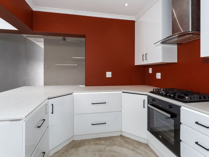 Modern kitchen featuring white cabinetry, stone countertops, a gas hob, and a built-in oven, set against a bold red feature wall.