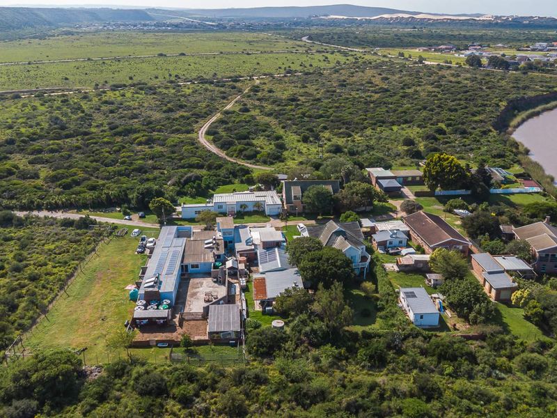 An aerial view of the property complex, showcasing multiple buildings, roof-mounted solar panels, water storage tanks, and surrounding natural landscape near the river.