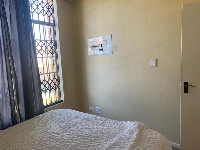 A bedroom featuring a window with a security gate, an electrical distribution board, and standard electrical fixtures.
