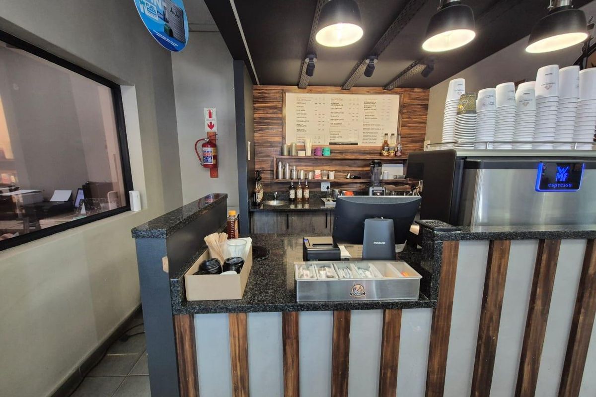 A functional coffee service counter featuring granite countertops, wood-panelled cladding, integrated shelving, and professional espresso machine setup.