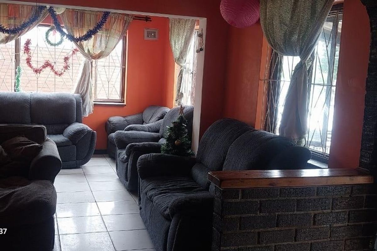 A living room area featuring tiled flooring and a brick feature wall, with security bars installed on the windows.