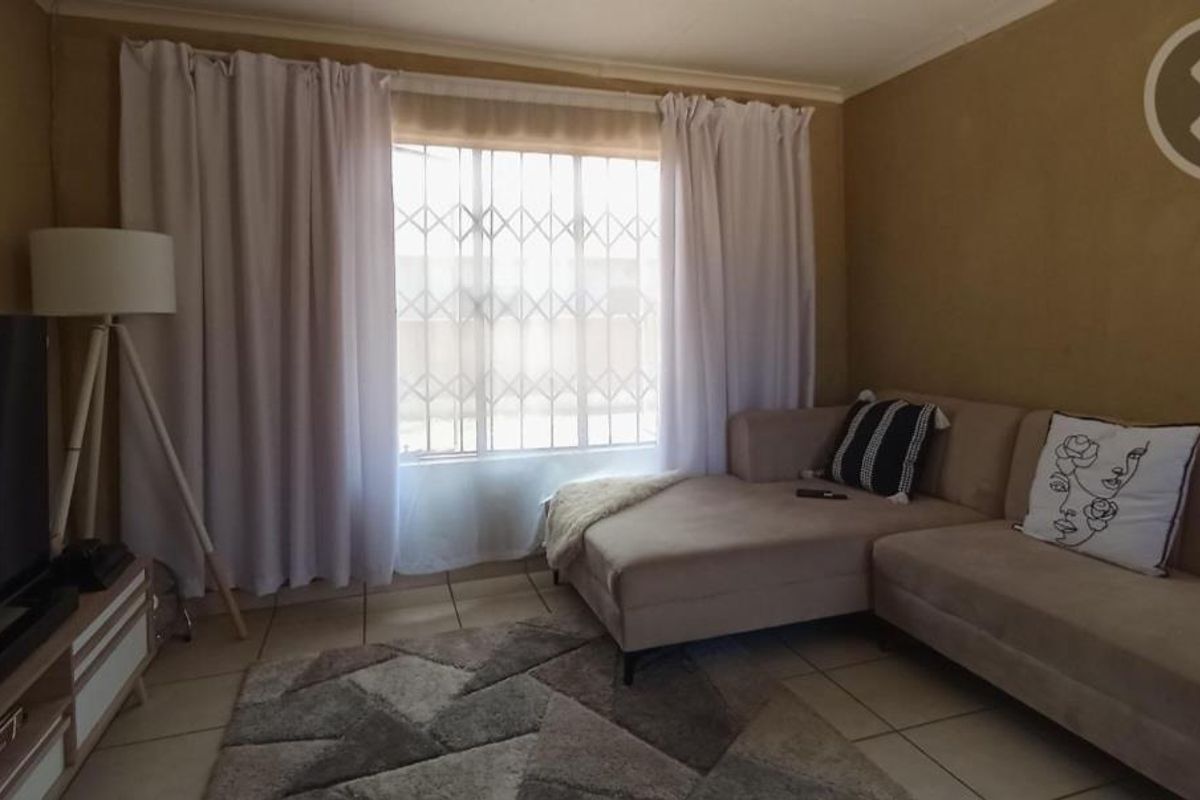 A cozy living room featuring tiled flooring, a large window with security bars, and neutral wall tones.