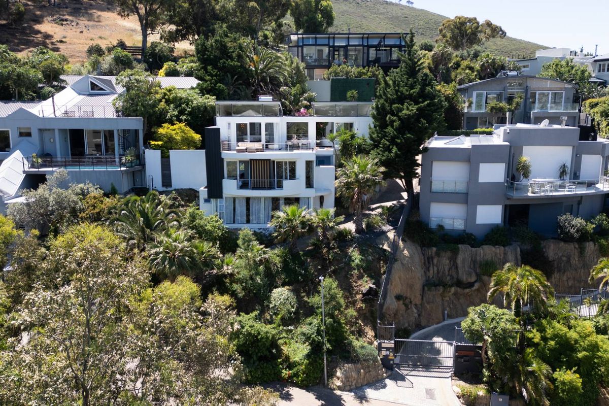 Aerial view of a multi-level residential property nestled on a hillside, featuring terraced landscaping, balconies, and a gated driveway entrance.