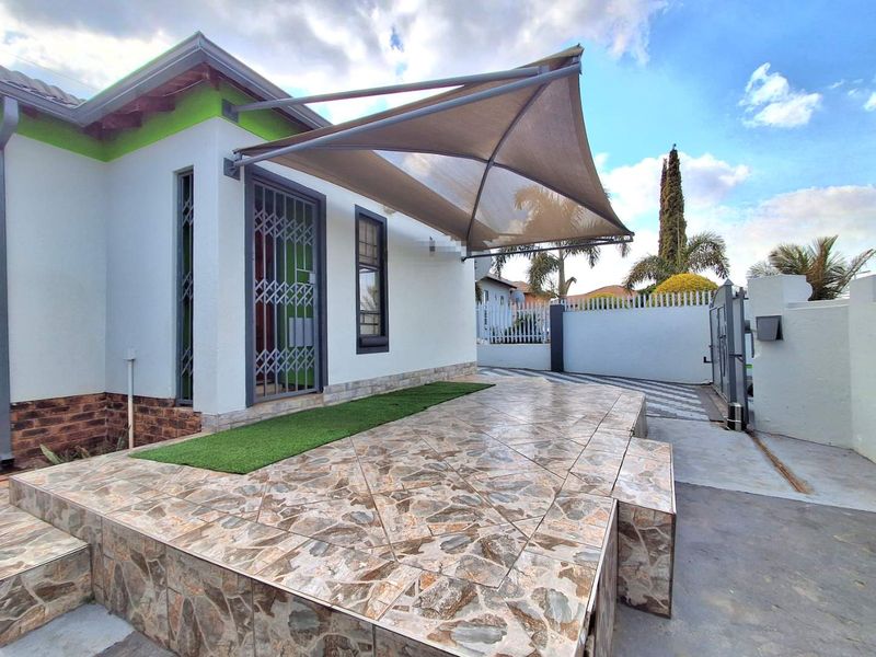A paved outdoor patio area featuring a modern shade sail, security gate, and low-maintenance artificial grass accents.