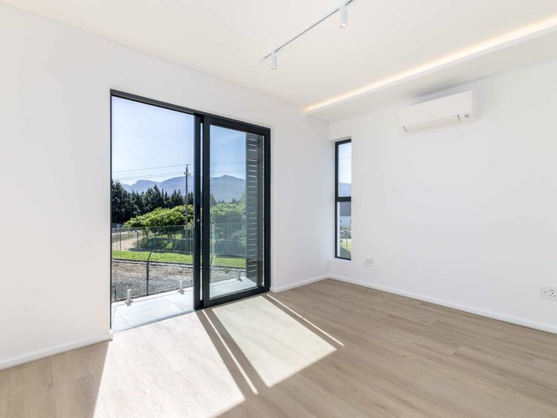 A bright, modern bedroom featuring light laminate flooring, an air conditioning unit, and a sliding glass door leading to a balcony with scenic views.