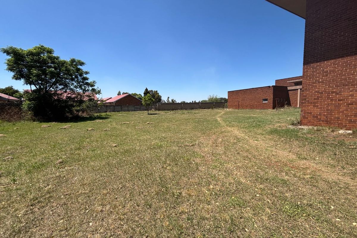 A view of the rear exterior area featuring a large grass lawn, perimeter wall, and face brick building facade.