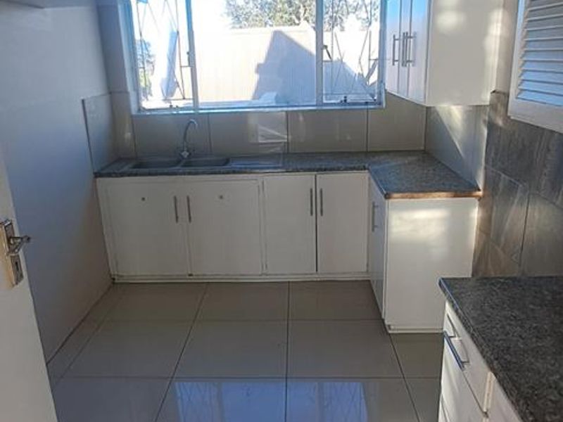 A functional kitchen featuring white built-in cabinetry, granite countertops, a double basin sink, and tiled flooring with natural light from the window.