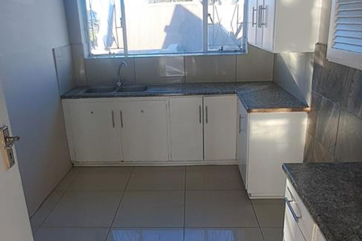 A functional kitchen featuring white built-in cabinetry, granite countertops, a double basin sink, and tiled flooring with natural light from the window.