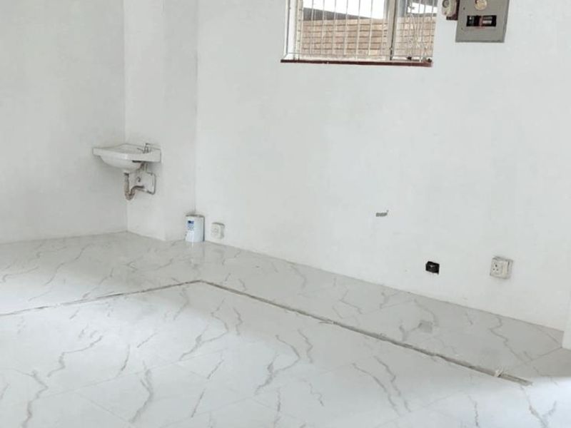 An empty office space featuring marble-look tiled flooring, a wall-mounted basin, and security bars on the window, currently undergoing minor finishing work.