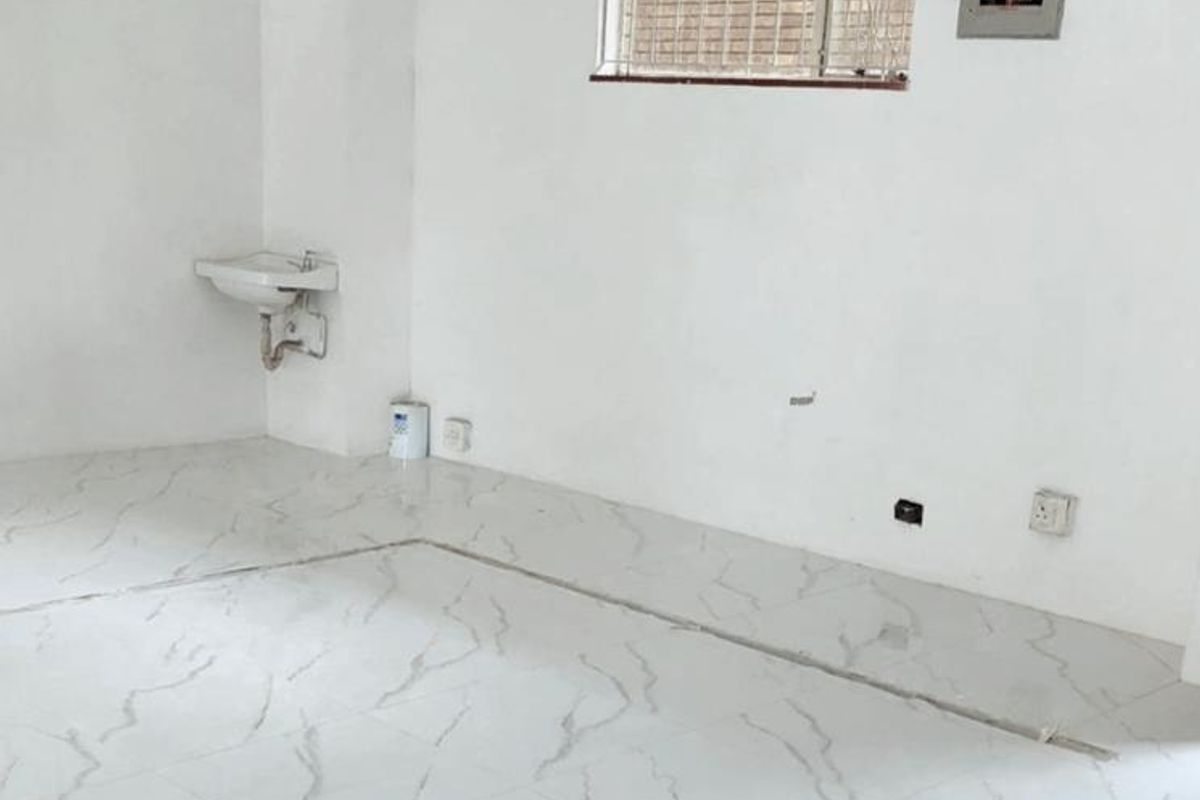 An empty office space featuring marble-look tiled flooring, a wall-mounted basin, and security bars on the window, currently undergoing minor finishing work.