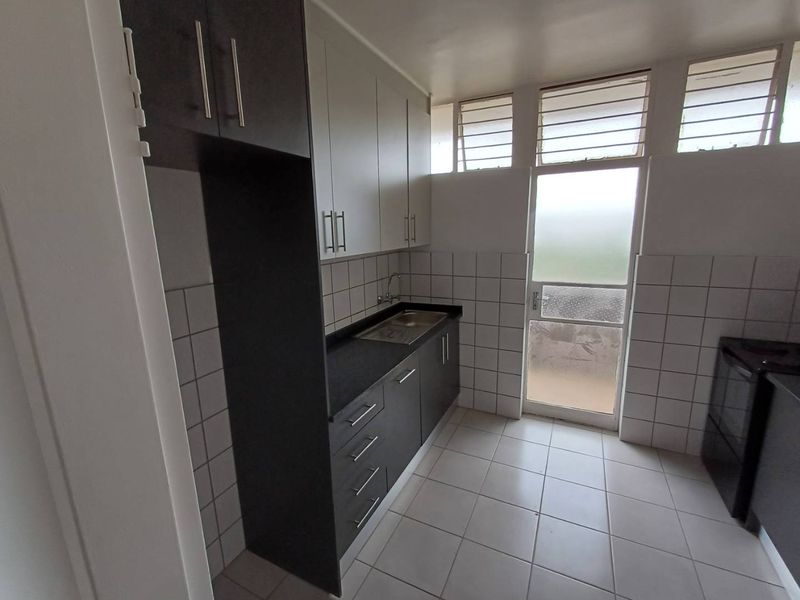 A clean, functional kitchen featuring dark cabinetry, contrasting countertops, tiled backsplash, and direct access to an outdoor area through a glass panel door.