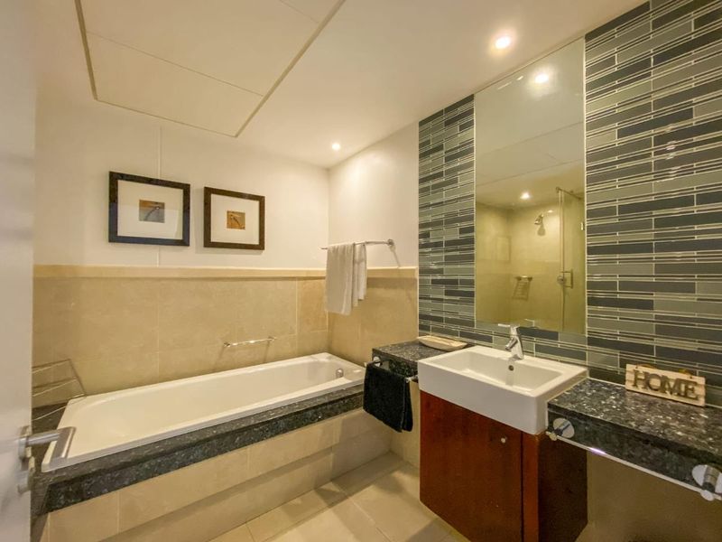 A well-appointed bathroom featuring a built-in bathtub, a vanity with a basin, and decorative tiled wall accents.