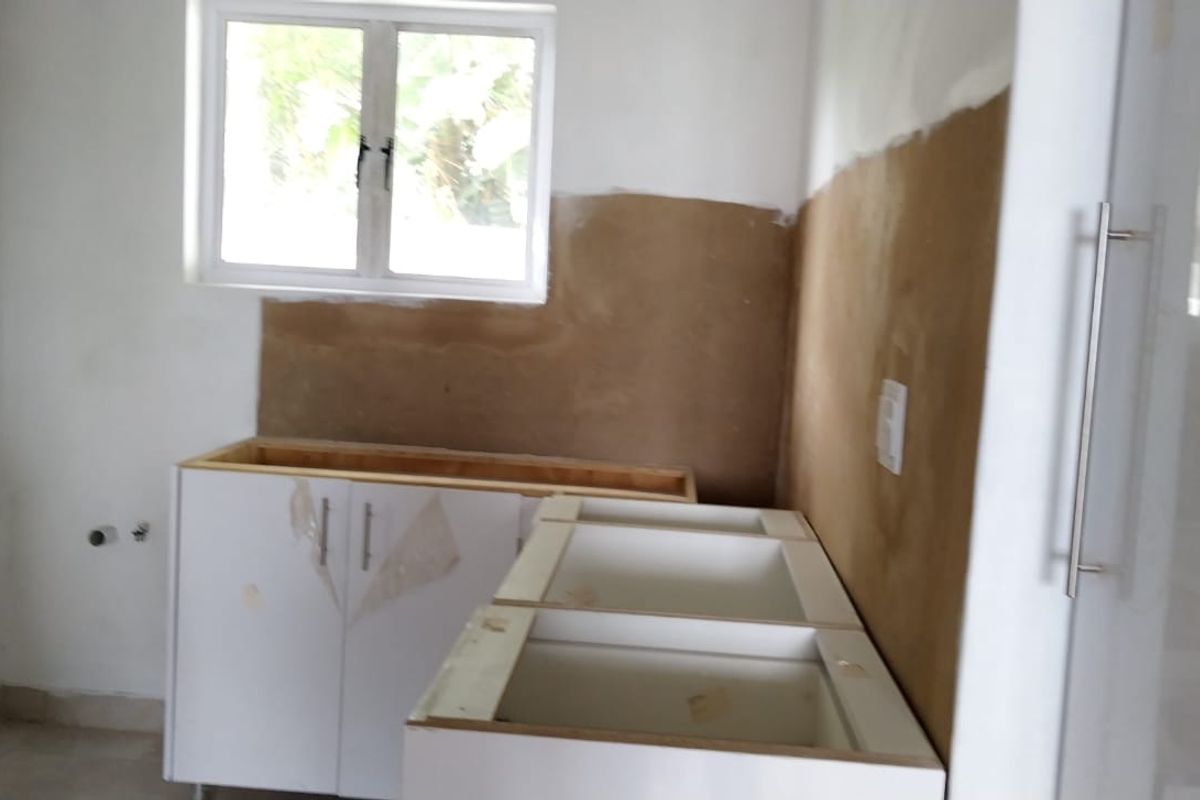 An unfinished kitchen area featuring base cabinetry, exposed wall surfaces, and a window, currently awaiting final installation and completion.