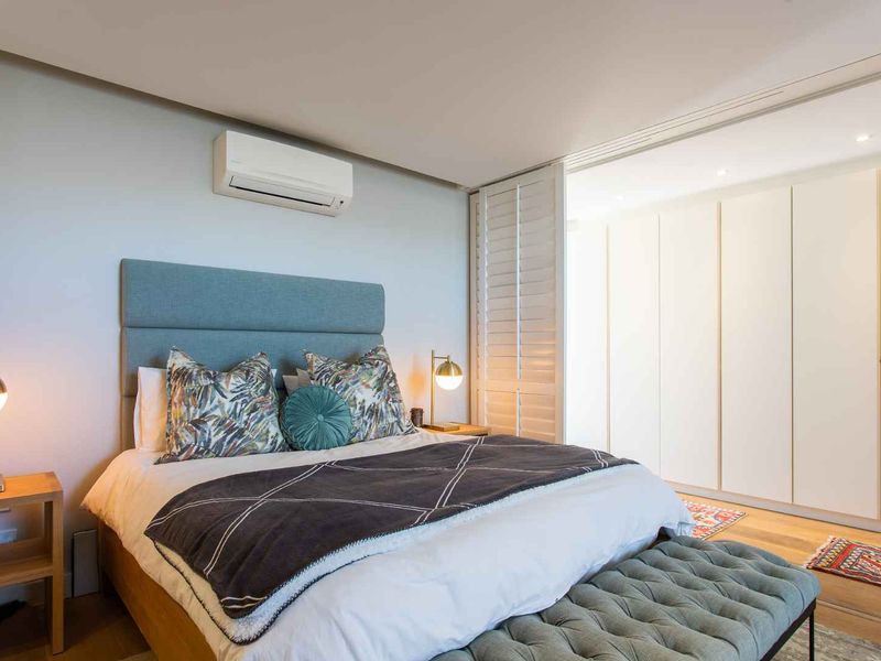 A well-maintained bedroom featuring timber flooring, built-in wardrobes, plantation shutters, and a wall-mounted split-system air conditioner.