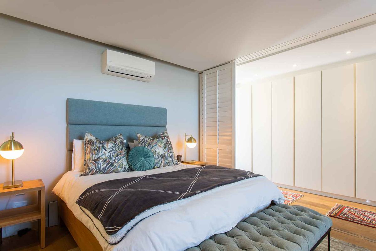 A well-maintained bedroom featuring timber flooring, built-in wardrobes, plantation shutters, and a wall-mounted split-system air conditioner.