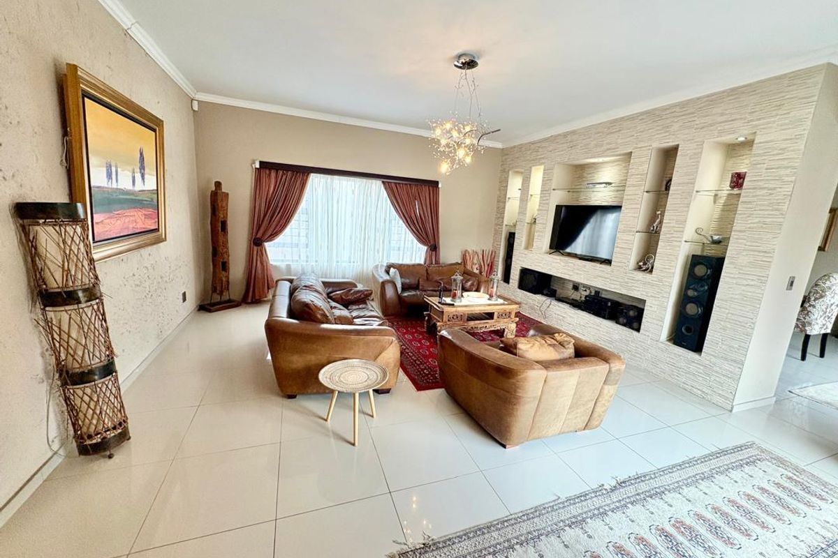 Spacious living room featuring large format floor tiles, a custom built-in media wall with recessed shelving, and elegant recessed lighting.