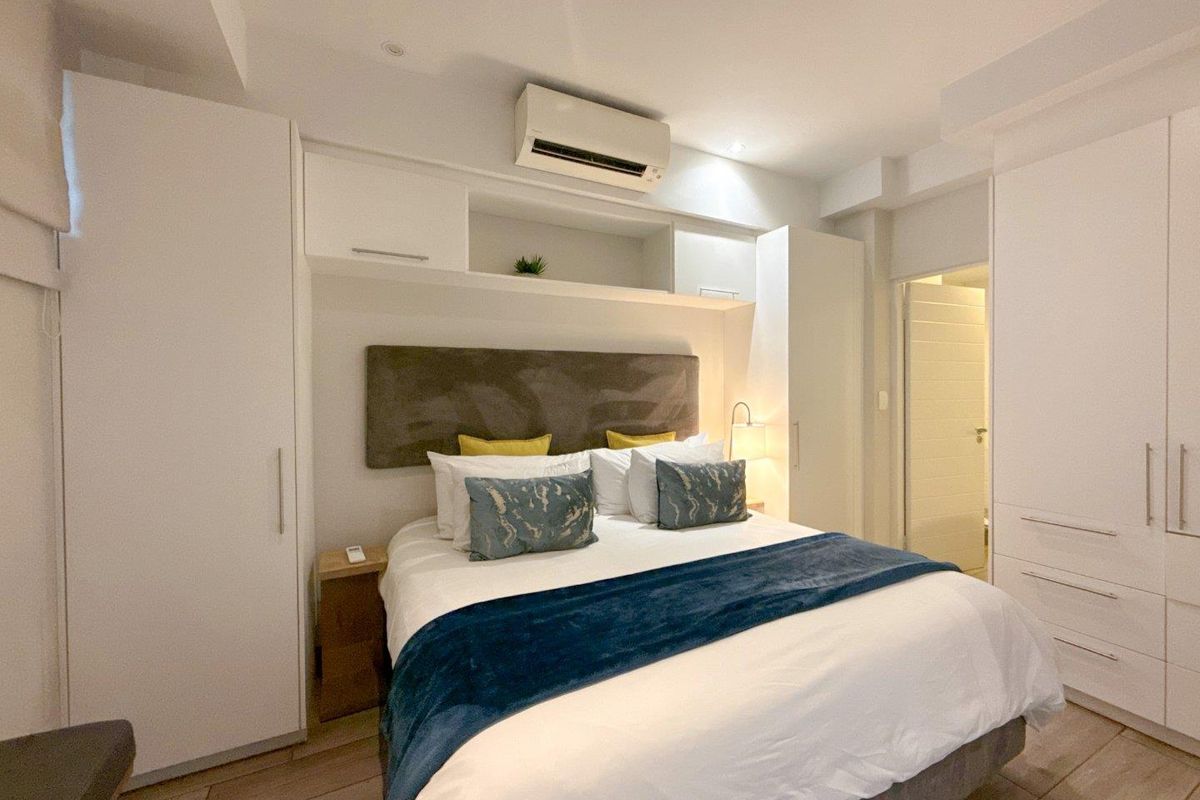 A well-maintained bedroom featuring extensive built-in white cabinetry, overhead storage, wall-mounted air conditioning, and modern tiled flooring.