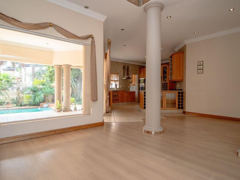 Spacious open-plan living area featuring laminate flooring, decorative columns, and a seamless transition to the kitchen, with large windows overlooking the pool area.