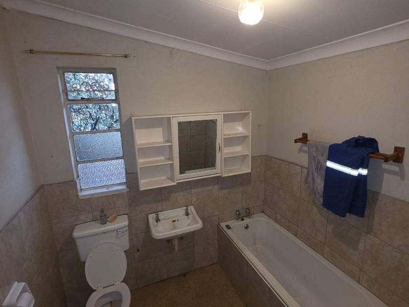 A functional bathroom featuring a built-in bathtub, wall-mounted basin, and toilet, with tiled wall finishes and a medicine cabinet.