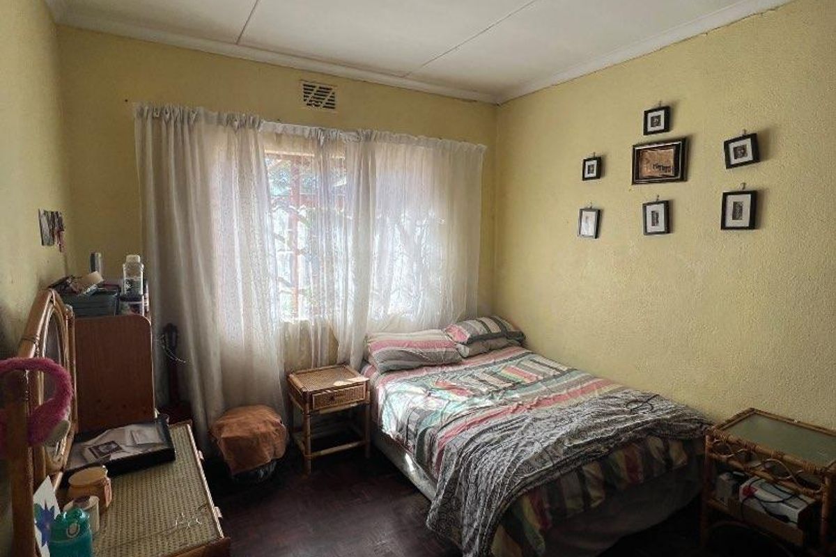 A compact bedroom featuring original parquet flooring, a central ceiling light fixture, and a window with curtain tracks.