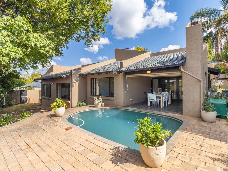 Rear view of the property featuring a covered patio, a swimming pool, and paved outdoor entertainment area surrounded by established garden.