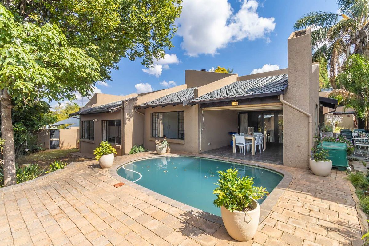 Rear view of the property featuring a covered patio, a swimming pool, and paved outdoor entertainment area surrounded by established garden.