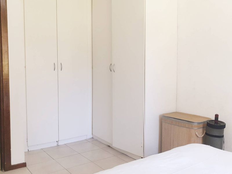 A bedroom featuring built-in cupboards and tiled flooring, with an adjacent view into a bathroom area.