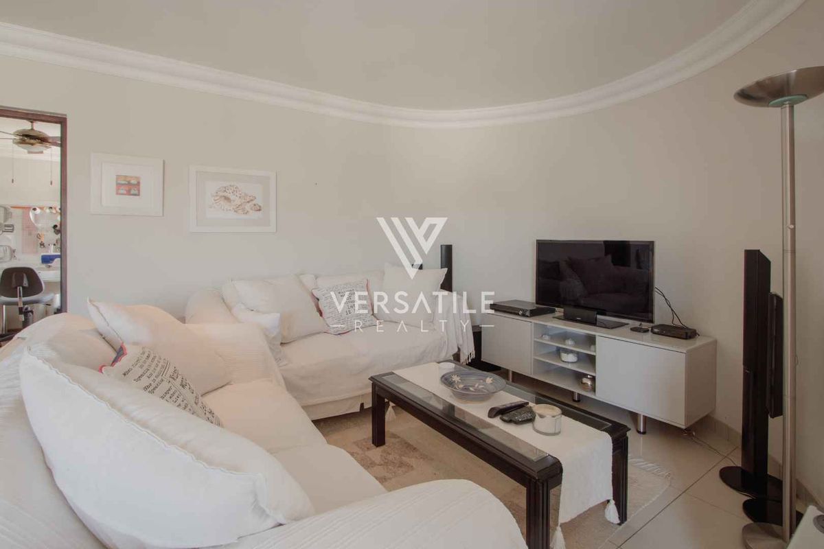 A comfortable living room featuring tiled flooring, coved ceiling detailing, and neutral wall finishes, providing a functional and inviting space.