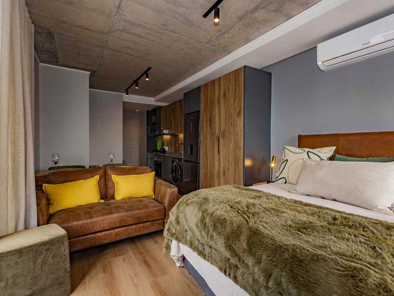 Modern open-plan studio apartment featuring an exposed concrete ceiling, sleek built-in cabinetry, integrated laundry appliances, and a wall-mounted air conditioning unit.