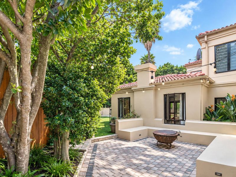 A well-maintained paved patio area featuring built-in seating, string lighting, and mature garden landscaping, perfect for outdoor entertaining.