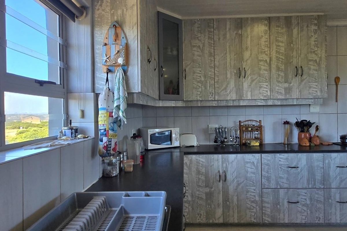 A functional kitchen featuring wood-look cabinetry, dark countertops, built-in oven, and large windows offering natural light and scenic views.