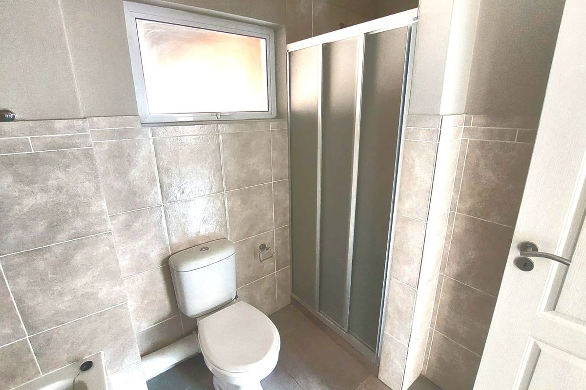 A functional bathroom featuring a tiled shower enclosure, a standard toilet, and a small window for natural light and ventilation.
