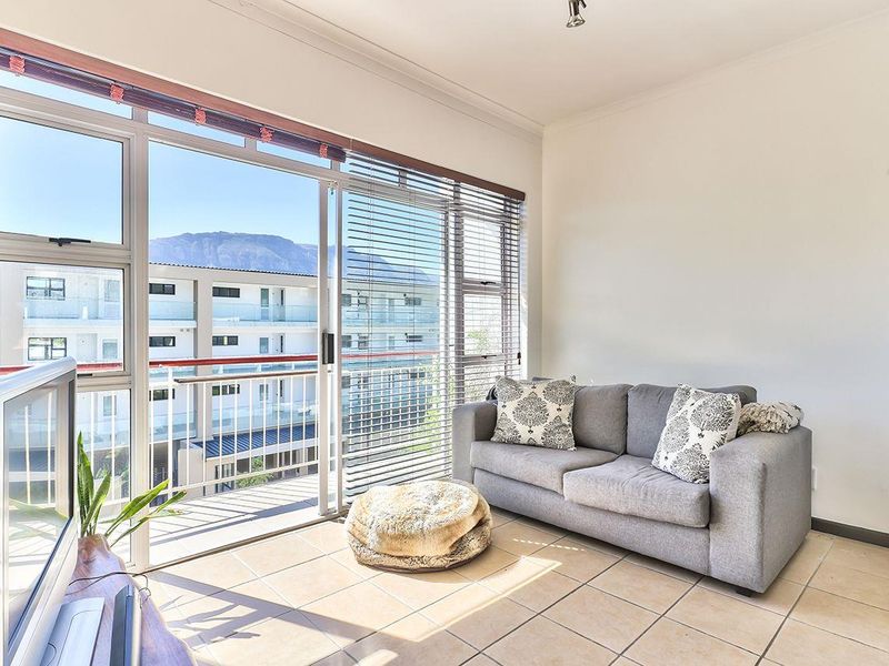 A bright living room featuring tiled flooring and large sliding glass doors that provide access to a balcony with mountain views.
