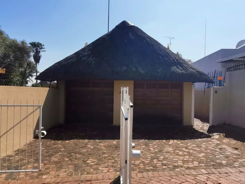 A detached double garage featuring a traditional thatched roof, set within a secure property with paved driveway and perimeter walling.