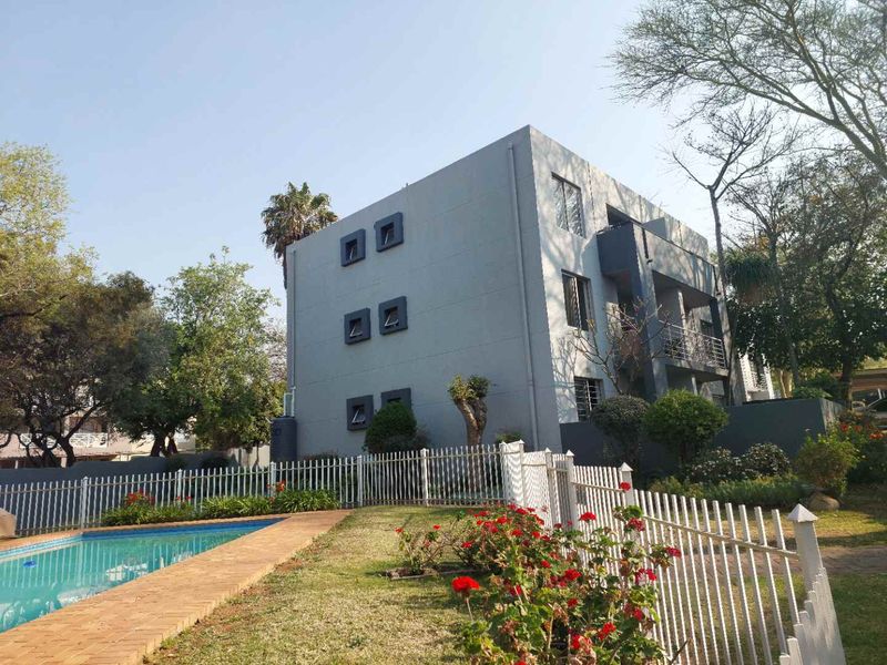 Exterior view of the apartment building featuring a swimming pool, landscaped garden area, and private balconies.