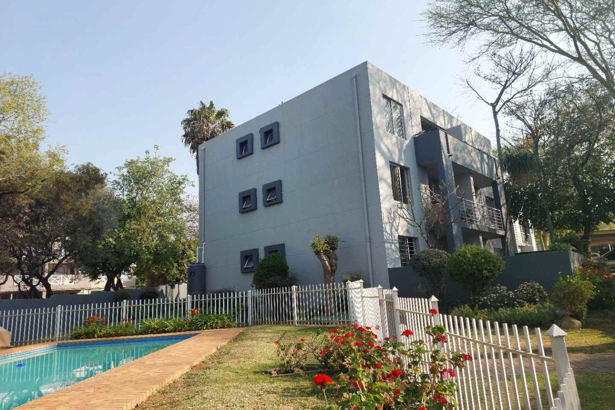 Exterior view of the apartment building featuring a swimming pool, landscaped garden area, and private balconies.