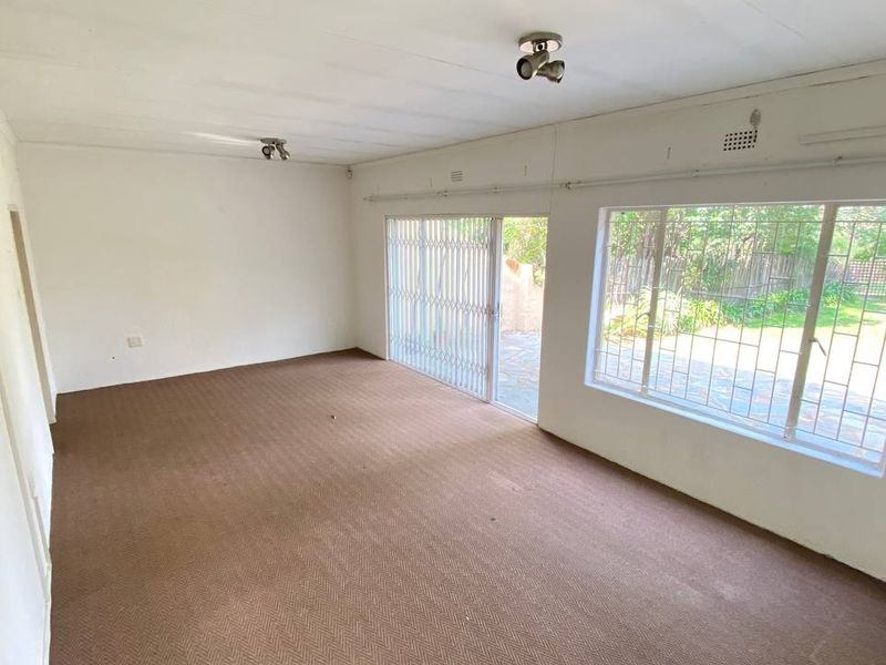 A spacious, empty living room featuring large windows with security bars and a sliding glass door leading to the garden area.